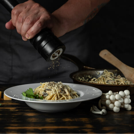 Chef hands adding paper in dish and cooking Italian pasta carbonara with parmesan cheese and white creamy sauce on wooden table background.
