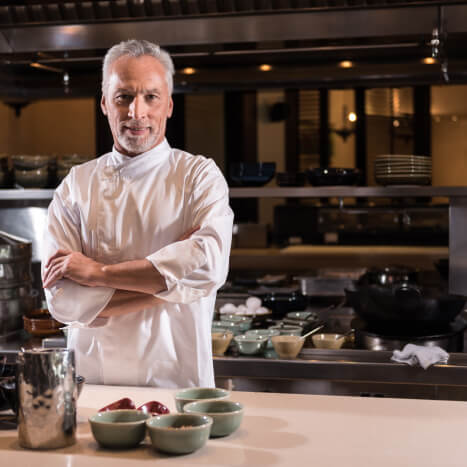 Delighted bearded chef standing in the kitchen of the restaurant